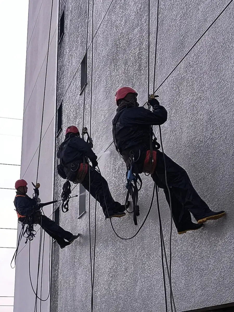 Equipe realizando manutenção de fachada com cordas